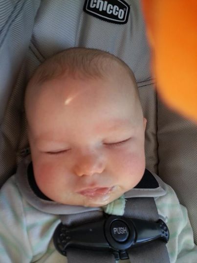 Milk-covered face and asleep in car seat.